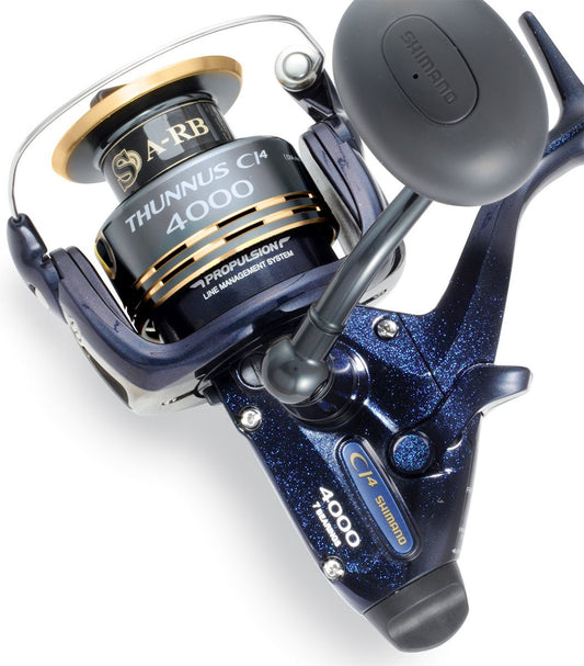 A close-up of the Shimano Thunnus 4000CI4 Saltwater Spinning Reel highlights its black and gold spool, ergonomic handle, metallic blue body, and prominent Shimano branding with model details.